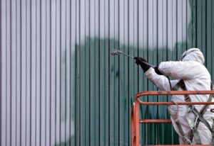 A commercial painter on an industrial lift spray painting a steel exterior wall or duct.