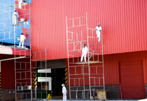 an industrial painter painting a building's exterior while on a scaffolding